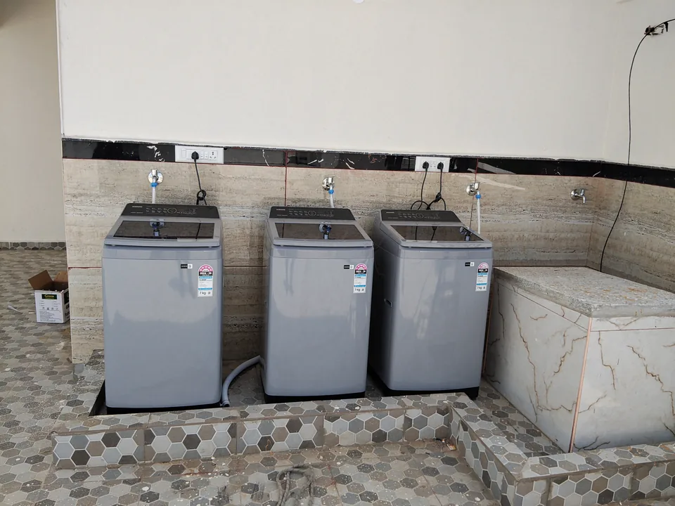 Three top-loading washing machines in a tiled utility area.